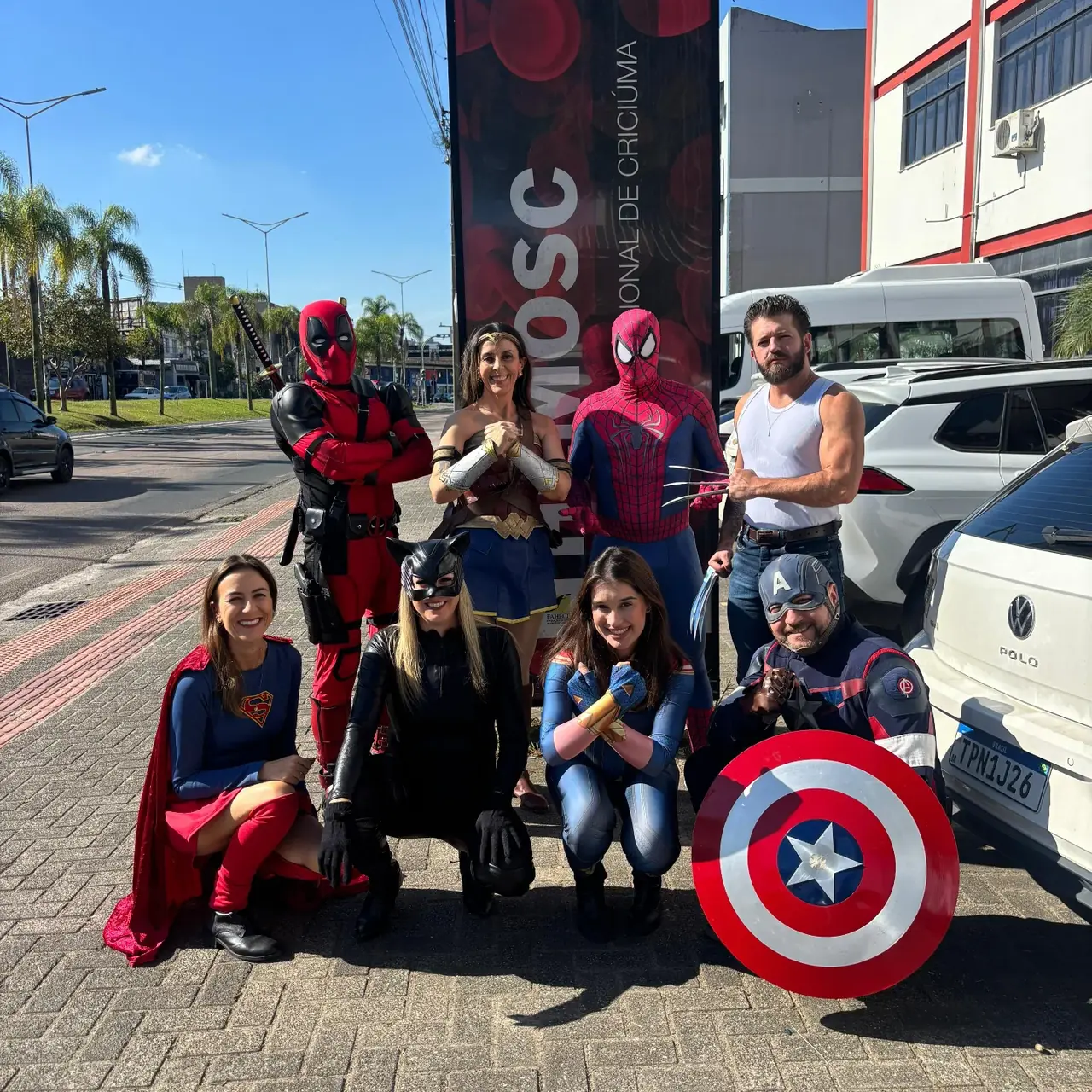 Equipe posando na rua, em frente ao banner da campanha HEMOSC